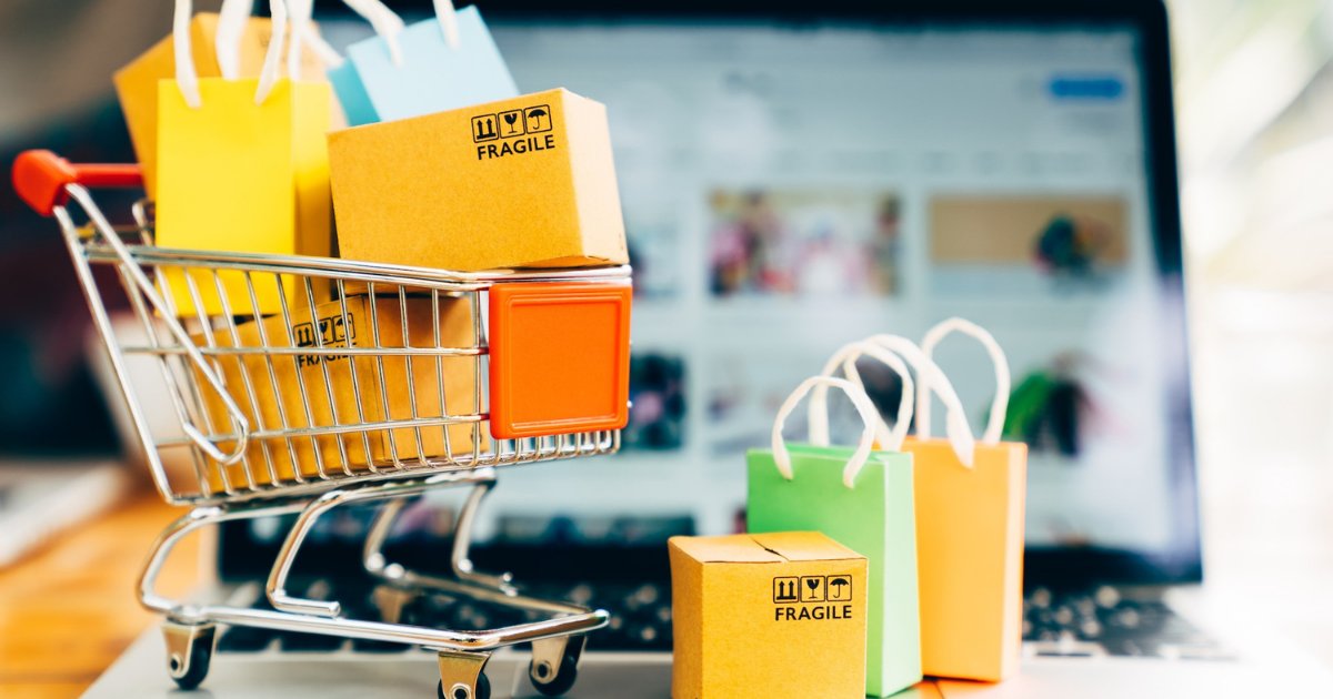 Carrinho de compras em miniatura com caixas e sacolas coloridas na frente de um notebook